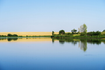 Reflection of the sky with clouds on the shore of a large lake on a sunny summer day.