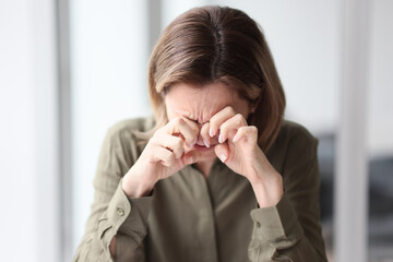 A woman sitting at a table in the office wipes her eyes