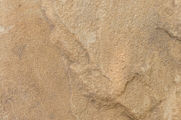 Stone wall is sand-colored with dark spots and bulges. Textured background of stone color sand close-up.