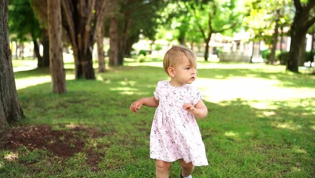 Little girl in a dress learns to walk in the park among the trees