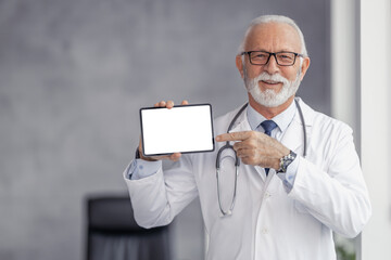Portrait of senior male doctor holding digital tablet and showing free space