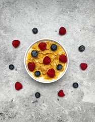 Corn flakes with berries and milk in white plate on light background.