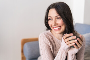 A happy young woman is sitting at home on the couch and looking at the camera. Portrait of a cozy woman resting in an armchair. Portrait of a beautiful smiling girl.