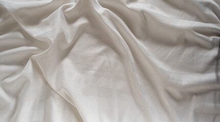 Satin crumpled fabric of light milky color, top view. Natural bed linen, sheets, abstract background of luxury fabric, wavy folds