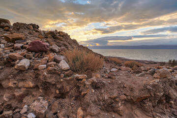 Dead sea shore at Jordan side, dry sand and rocks beach, sunset sky above calm water background