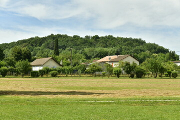 Obraz premium Pelouse séchée par le soleil devant quelques maisons et une colline boisée au bourg de Champagne au Périgord Vert 
