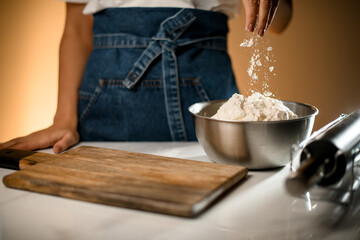 female hand pouring white flour in stainless bowl on table with modern kitchen appliances