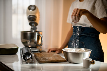 Selective focus on hand of woman gently pouring flour in bowl on table with kitchen appliances