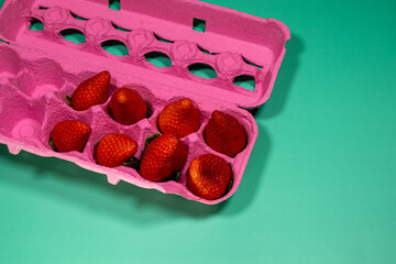 Healthy and Delicious Food: Close-up of Pink Egg Carton with Strawberries on Vibrant Green Background