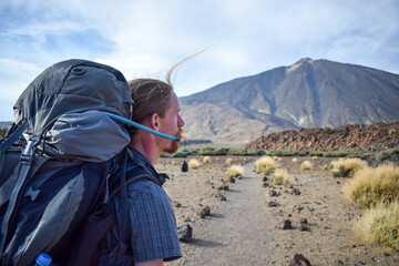 Handsome young traveler man hiking drinking water on mountain with Teide volcano on the background. Enjoying hot weather and sun in Spain. Staying hydrated on sport hike. Hydration bladder. - obrazy, fototapety, plakaty