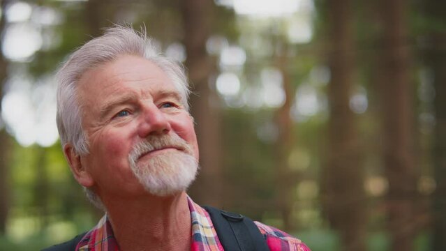 Portrait of smiling active senior man with backpack on hike through woodland countryside enjoying peace and beauty of nature- shot in slow motion