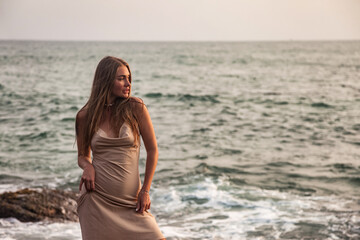 Fototapeta na wymiar Pretty young lady in beige dress relaxing on beach at tropical ocean background, looking away. Cute slender woman enjoy rest on seacoast. Travel vacation holiday concept. Copy advertising text space