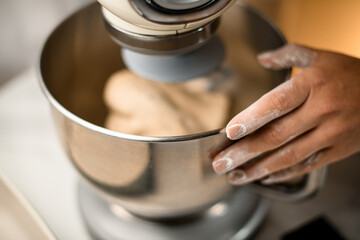 selective focus on female hand in flour at stainless bowl of modern kitchen mixer.