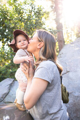 woman holding and kissing a baby with a sun hat in the park