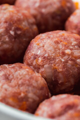 Homemade meatballs with tomato sauce, carrot and spices. Raw ground beef meatballs with rice in a white dish for baking. White marble background. Original way to cook meat