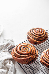 Sweet twisted buns with poppy seeds on cooling rack on white background with copy space