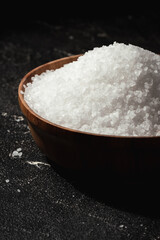 Coarse white salt in a wooden bowl on the black background