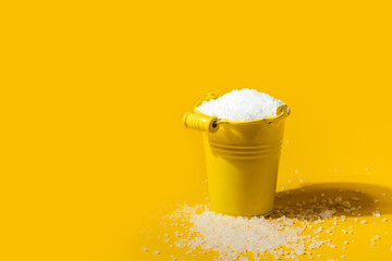 Coarse white salt in a yellow metal small bucket on the yellow background. Free space for text