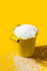 Coarse white salt in a yellow metal small bucket on the yellow background. Free space for text
