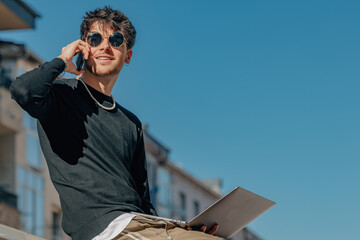 young man with sunglasses and computer talking on mobile phone outdoors