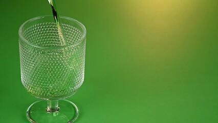 glass being filled with green alcoholic drink with emerald theme background for st patricks day celebration. Irish holiday is popular drinking event when people party and consume large quantities