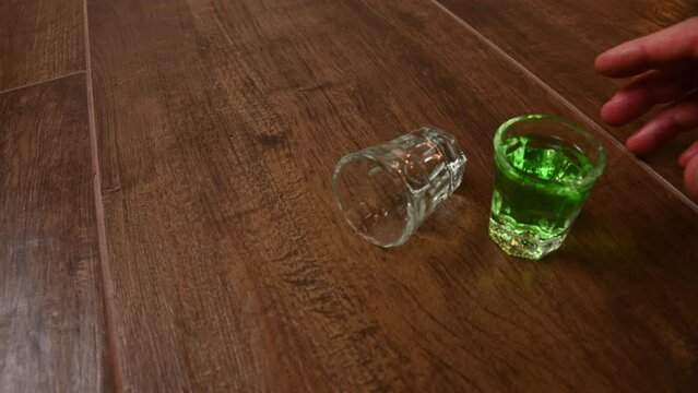 deliberately unstable shaky to simulate drunk POV style. shot and pint glasses on wooden bar background filled with green spirit cocktail and shamrock, drunk at celebration for St Patrick's day 2023. 