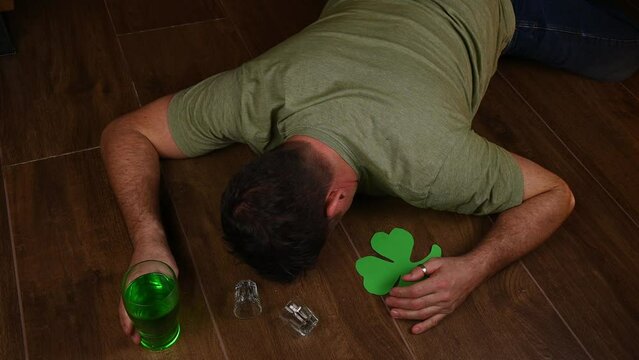 excessive alcohol drinking has left this Irish party animal wasted blackout drunk after heavy binge drinking for St Patricks day celebrations. Pint of green drink and empty shot glasses remain