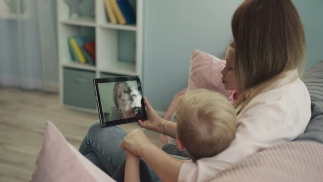 Grandma talks to grandchildren and daughter on video call via tablet. Woman holds modern gadget letting kids to see granny on screen closeup