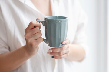 Closeup of female hands with a mug of beverage. Beautiful girl holding cup of tea or coffee in the morning.