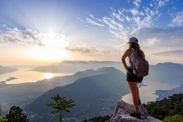 Happy girl with a backpack is on the edge of a high mountain in Montenegro