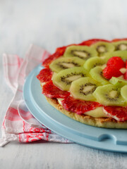 Homemade cake with strawberries, kiwi, red orange and cream on a blue background, fruit tart, pastry shop, desserts, sweets, close-up.