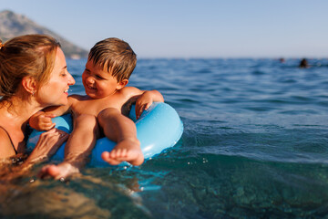 Caring mother rides her son on an inflatable ring in the sea