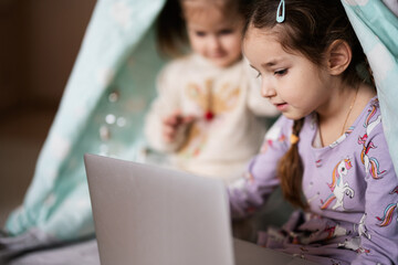 Two girls sisters watching on laptop at wigwam tent. Technology and home concept. © AS Photo Family