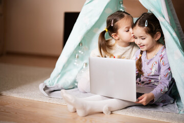 Two girls sisters watching on laptop at wigwam tent. Technology and home concept. © AS Photo Family