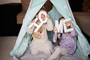 Two girls sisters at wigwam tent with wooden home letters. © AS Photo Family