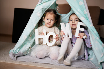 Two girls sisters at wigwam tent with wooden home letters. © AS Photo Family