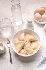 Fresh boiled dumplings in a light plate on a light background. Pattern, background. Homemade craft production, national traditions, Ukrainian cuisine