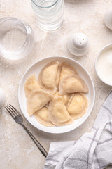 Fresh boiled dumplings in a light plate on a light background. Pattern, background. Homemade craft production, national traditions, Ukrainian cuisine
