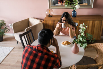 Young diverse loving couple eating croissant and talks together at home in breakfast time. Communication and relationship concept