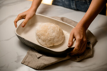 close-up top view of raw dough in a ceramic baking dish on the table and female hands