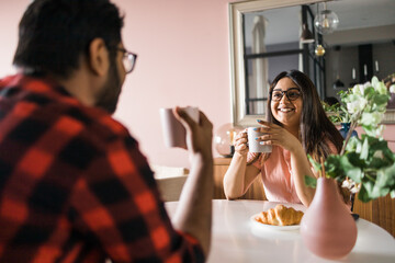 Young diverse loving couple eating croissant and talks together at home in breakfast time. Communication and relationship concept