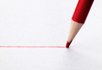 Draw a line on white paper with a red pencil. Close up. Macro