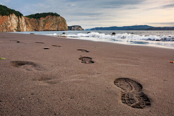 Footprints in the sand, Pacific coast, rocks, mountains, waves, sunset. Kamchatka.