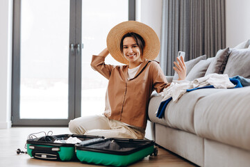 Happy blogger girl with a hat shows her followers how she is packing her suitcase for vacation. Relaxation concept.