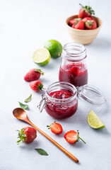 Homemade strawberry jam. Preserved food in a glass jar with fresh organic berries on a light background with lime. Eco-friendly  farm products.
