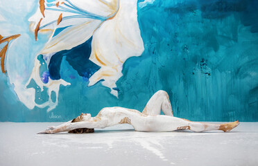 Young sexy nude woman lies with tension on the studio floor, doused with shiny wet white paint...
