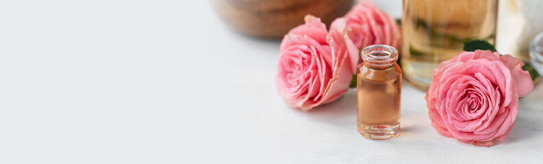 Obraz na płótnie Canvas Aromatherapy. Pure organic essential rose oil concept. Elixir with plant based floral herbal ingredients. Pink flowers extract. Spa atmosphere with candle, towel. White background. Banner copy space