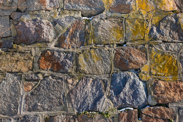 Wall of large granite stones held together with cement close-up on a sunny day. Natural background
