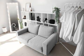 Interior of light dressing room with sofa, shelving unit and clothes