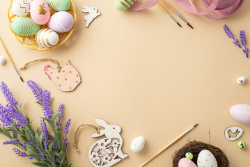 Easter concept. Top view photo of paintbrushes colorful easter eggs in bowl wooden bunnies chicken pink ribbon nest and lavender flowers on isolated beige background with copyspace in the middle